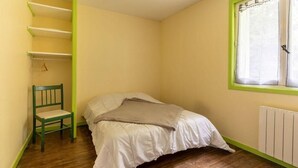 Ein Schlafzimmer mit Bett, Sessel, Fenster und Heizkörper.