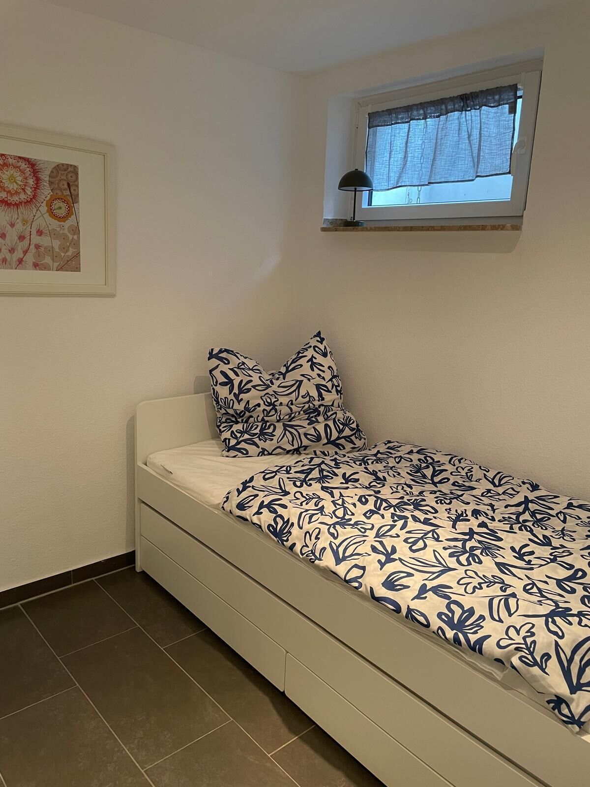 A bedroom with a bed, a window with a curtain, and a wall-mounted artwork.