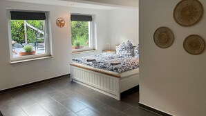 A bedroom with a bed, two windows, a view of greenery, and three wall-mounted decorative items. - Nideggen's Schwedenhaus, right next to the forest with great hiking trails and a fireplace. (Nideggen)