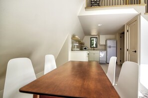 A dining area with a wooden table and white chairs, a kitchen with white cabinets, and a balcony with a wooden railing.