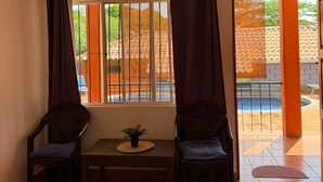 A room with two chairs, a small table, and a bed. There is a window with curtains and a view of a swimming pool outside. - Bolimar Collection at Playa Hermosa - N4 (Playa Hermosa)
