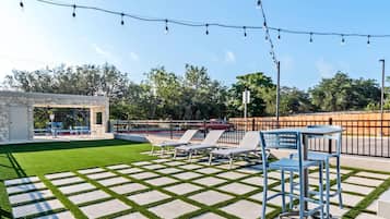 A patio area with a stone-tiled floor, a small stone structure, and blue chairs.