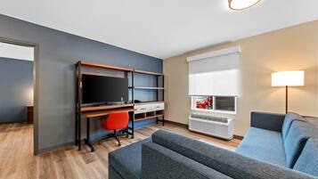 Ein modernes Wohnzimmer mit grauem Sofa, einem Holztisch mit Fernseher, einem roten Bürostuhl und einem Fenster mit Jalousien.