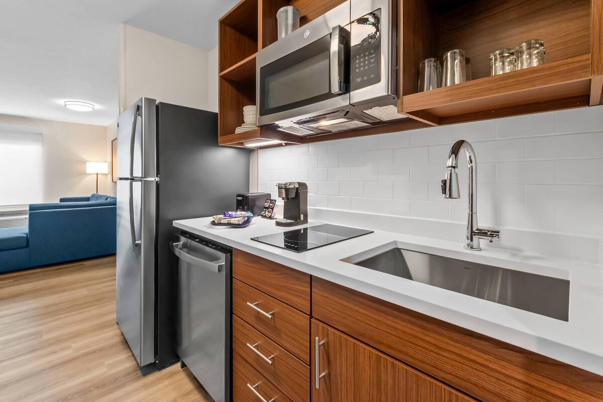 A modern kitchen with a stainless steel refrigerator, a microwave, and a sink. There is a coffee maker and a toaster on the countertop.