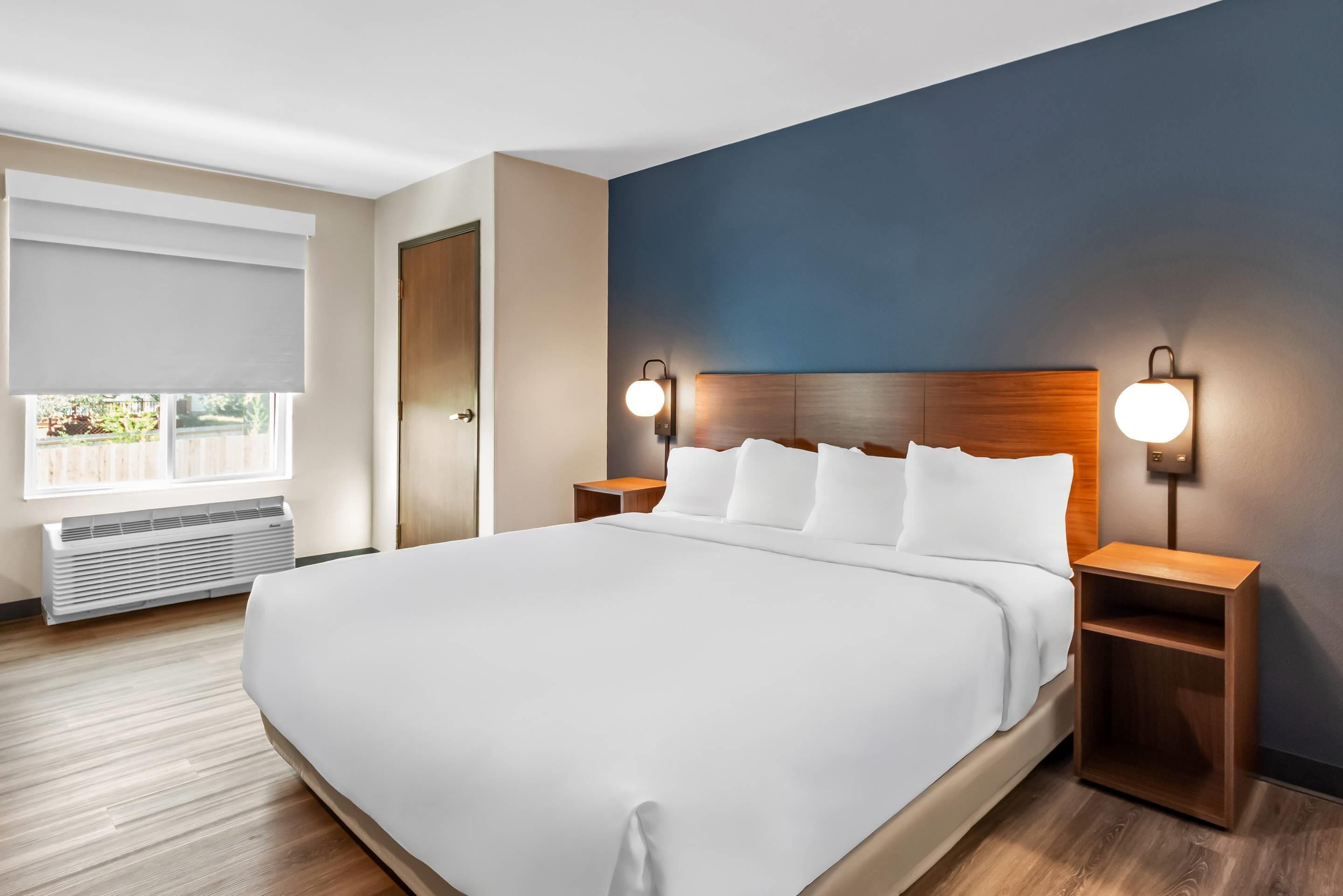 Una camera d'albergo moderna con un letto grande, due comodini, una finestra con tende e un lampadario a parete.