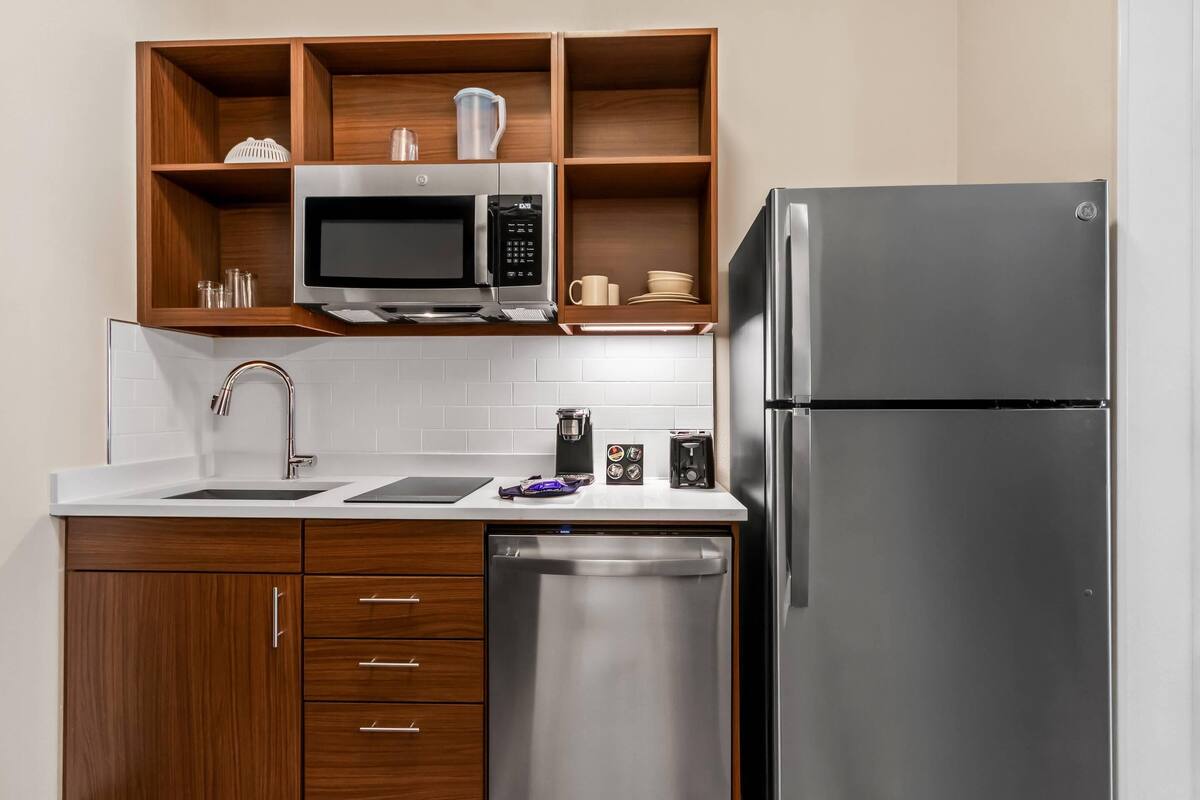 A modern kitchen with wooden cabinets, a stainless steel refrigerator, a microwave, and a dishwasher.