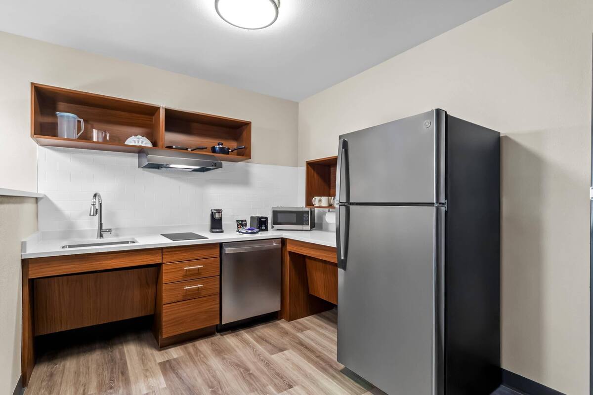 A modern kitchen with wooden cabinets, a stainless steel refrigerator, a microwave, and a dishwasher.