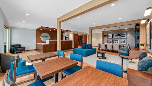 Un hall d'hôtel moderne, doté de meubles en bois, de sièges bleus et d'un espace de réception sur lequel est affiché un panneau indiquant « EVERHOME SUITES ».