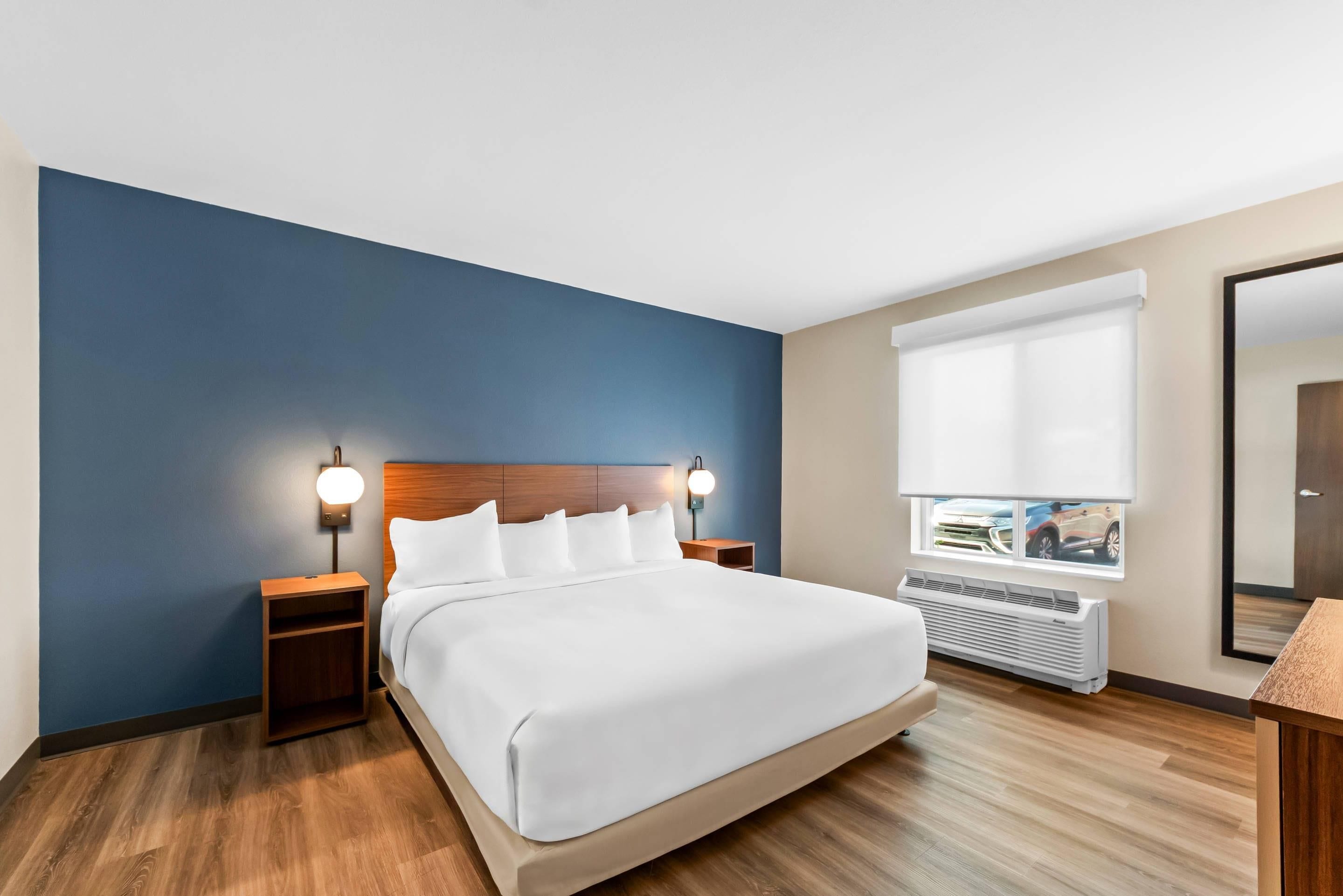 Une chambre d’hôtel avec un grand lit, deux tables de chevet avec des lampes, une fenêtre avec des stores et un radiateur.