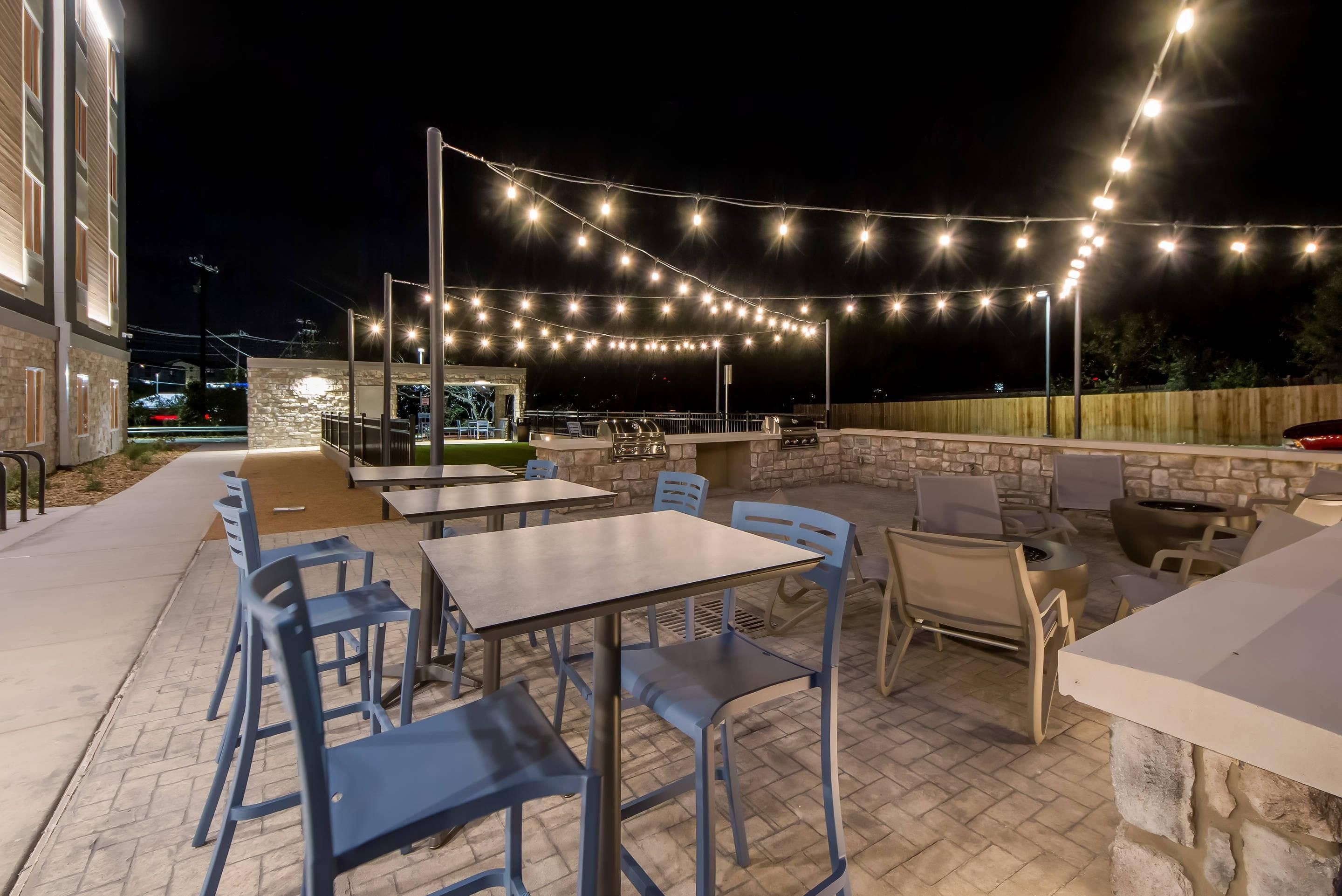 Un patio al aire libre con mesas y sillas, luces colgantes y una pared de piedra.