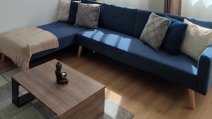 Un salon moderne avec un canapé d’angle, une table basse en bois et de grandes fenêtres avec des rideaux.