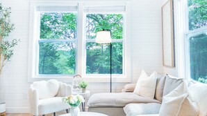 Una sala de estar acogedora con una mesita redonda, dos sofás y ventanas amplias con vistas a la vegetación.