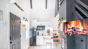 Una cocina moderna con armarios blancos, un refrigerador negro y una pantalla grande mostrando un fuego.