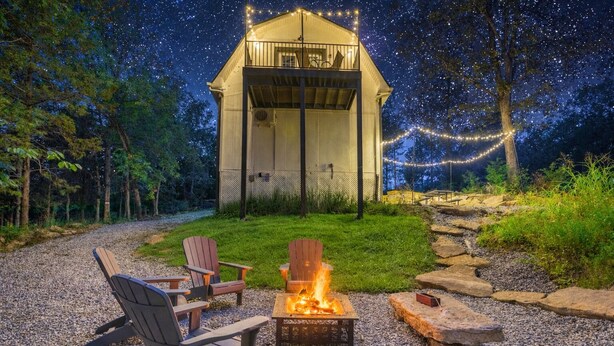Un espacio exterior acogedor con sillas Adirondack y una hoguera, rodeado por un sendero de grava y una terraza de madera.