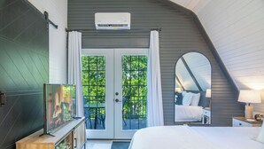 Un dormitorio con una cama, un televisor sobre un mueble de madera, un espejo y una ventana con cortinas.