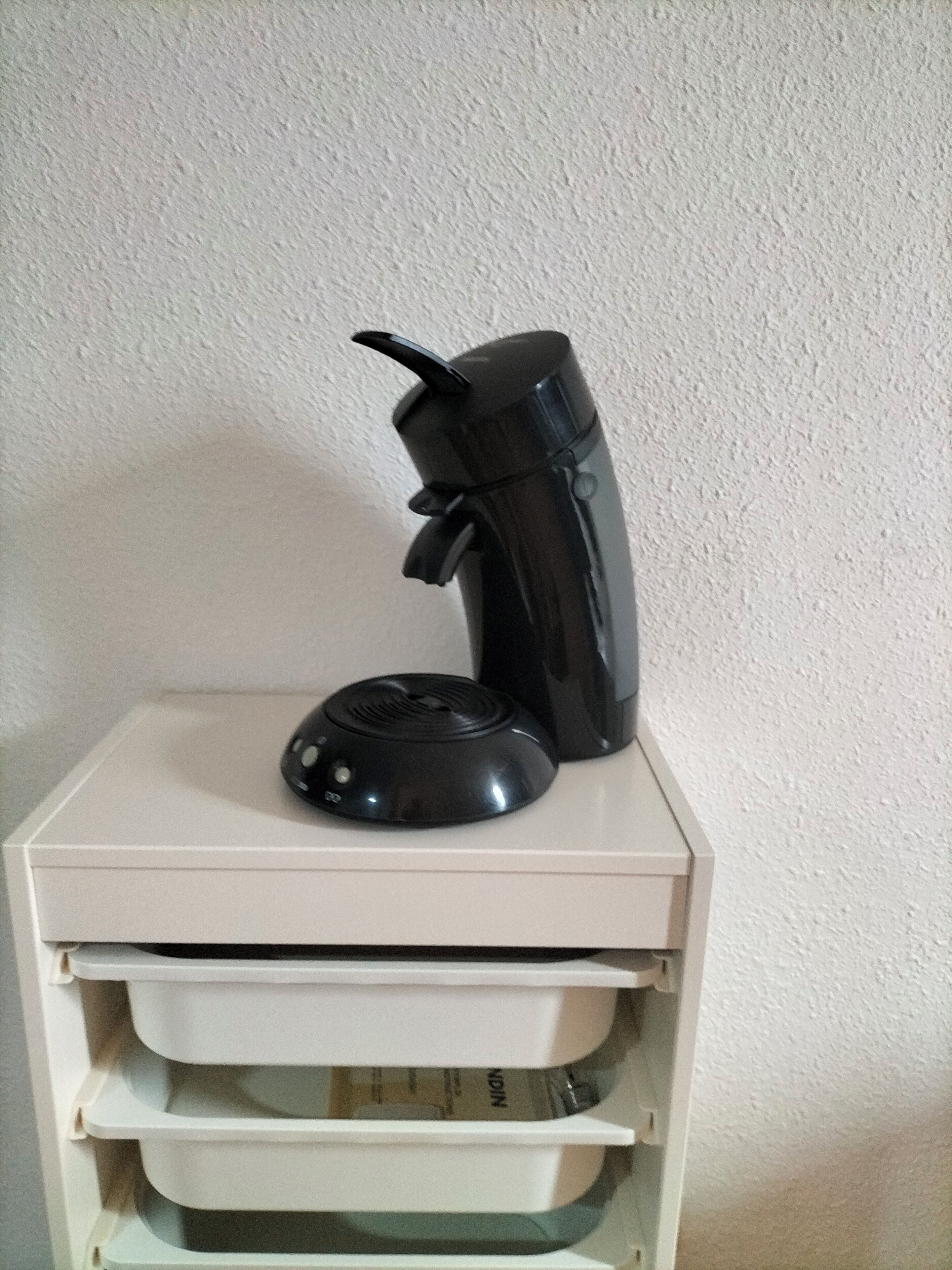 A black coffee maker on a white cabinet with multiple drawers.
