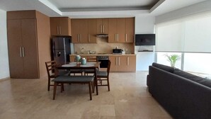 Eine moderne Küche mit Holzschränken, einem Esstisch mit Stühlen, einem schwarzen Sofa und einem an der Wand befestigten Fernseher.