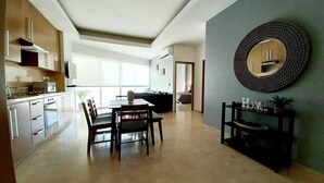 Eine moderne Küche mit integrierten Geräten, eine Essecke mit Tisch und Stühlen sowie ein Wohnbereich mit einer Couch und einem runden Spiegel an der Wand.