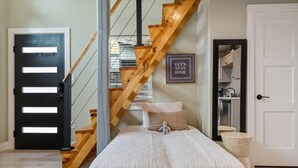 Une chambre avec un lit, un escalier en bois, une porte noire et un panneau encadré sur lequel on peut lire : « Restons chez nous ».