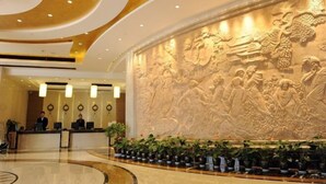 A hotel reception area with a large wall mural, a reception desk, and a row of potted plants. - Guangsha Hotel (Shengzhou)