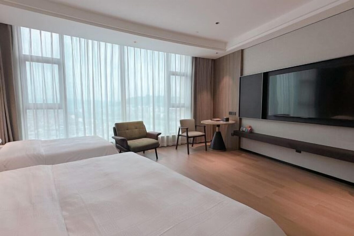 A hotel room with two beds, a TV, a small table, and a chair.