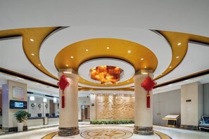 A hotel lobby with a central circular light fixture, columns with red decorations, and a patterned floor design. - Guangsha Hotel (Shengzhou)