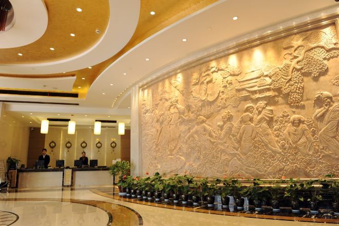 Vestíbulo de hotel con un mural grande e iluminado, una recepción y una zona de estar circular con plantas.
