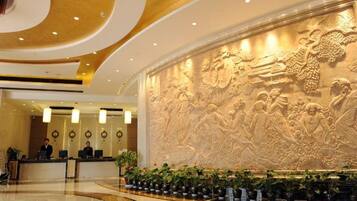 Vestíbulo de hotel con un mural grande e iluminado, una recepción y una zona de estar circular con plantas.