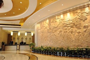 Vestíbulo de hotel con un mural grande e iluminado, una recepción y una zona de estar circular con plantas.