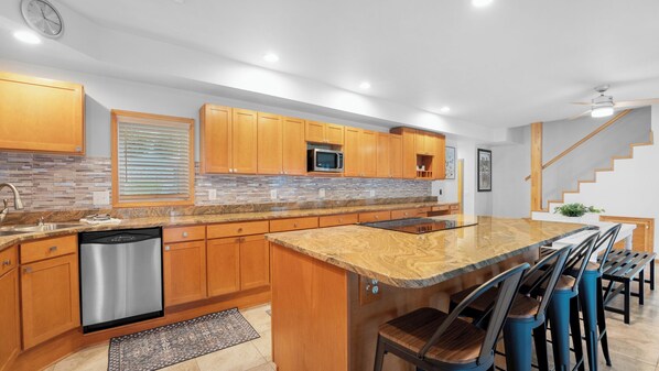 Una cocina moderna con armarios de madera, lavavajillas de acero inoxidable, microondas y una isla grande con taburetes de bar.