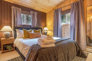 Une chambre à coucher aux murs lambrés, avec un lit, deux tables de chevet, des lampes et une fenêtre avec des rideaux.