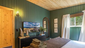 Un dormitorio con cama, cómoda, un cuadro y ventana con cortinas.