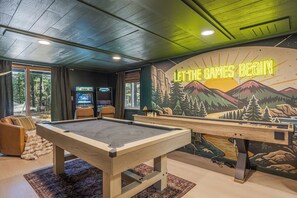Une table de billard dans une pièce ornée d’une fresque murale et d’un panneau néon sur lequel on peut lire : « QUE LES JEUX COMMENCENT ».