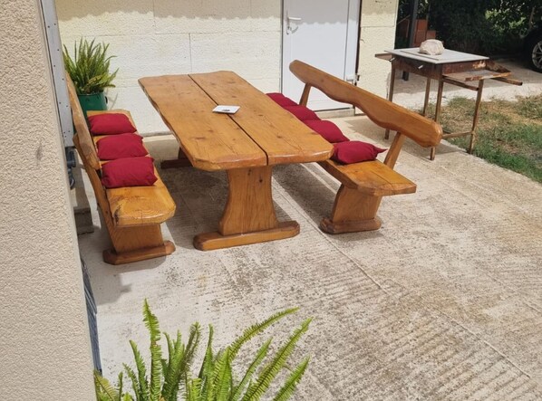 Un conjunto de comedor exterior de madera con bancos y una mesa, acompañado de cojines rojos.