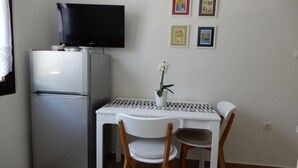 A compact kitchenette with a refrigerator, a small table, two chairs, and a potted orchid.