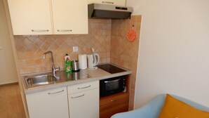 A compact kitchen with a sink, microwave, and storage cabinets. A blue sofa with a floral pillow is in the adjacent living area.