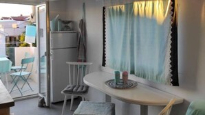 A small, open-plan living space with a kitchenette, a dining area, and a window with curtains.