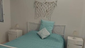 A bedroom with a bed, two bedside tables, and a wall-mounted macrame decoration.