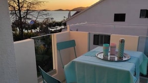A balcony with a table set for two, chairs, and a view of the sea and mountains.