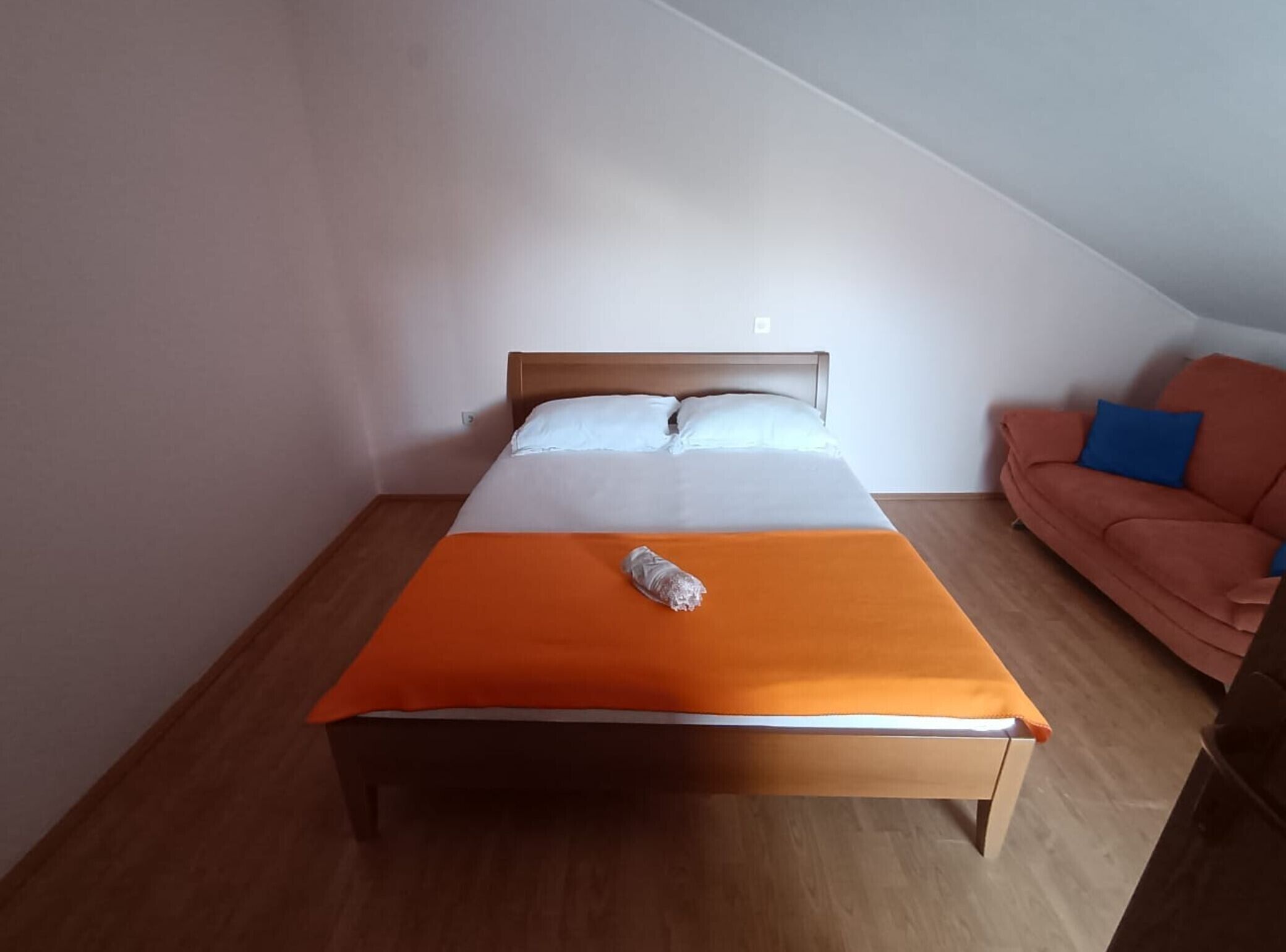 A single bed with an orange bedspread in a room with wooden flooring and a sloped ceiling.