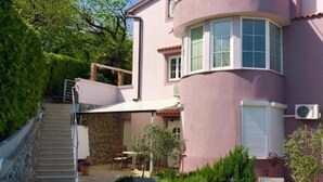 A two-story house with a stone staircase leading to a balcony, outdoor seating area, and a covered patio.