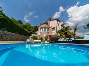 A large house with a swimming pool, surrounded by palm trees and a stone wall.