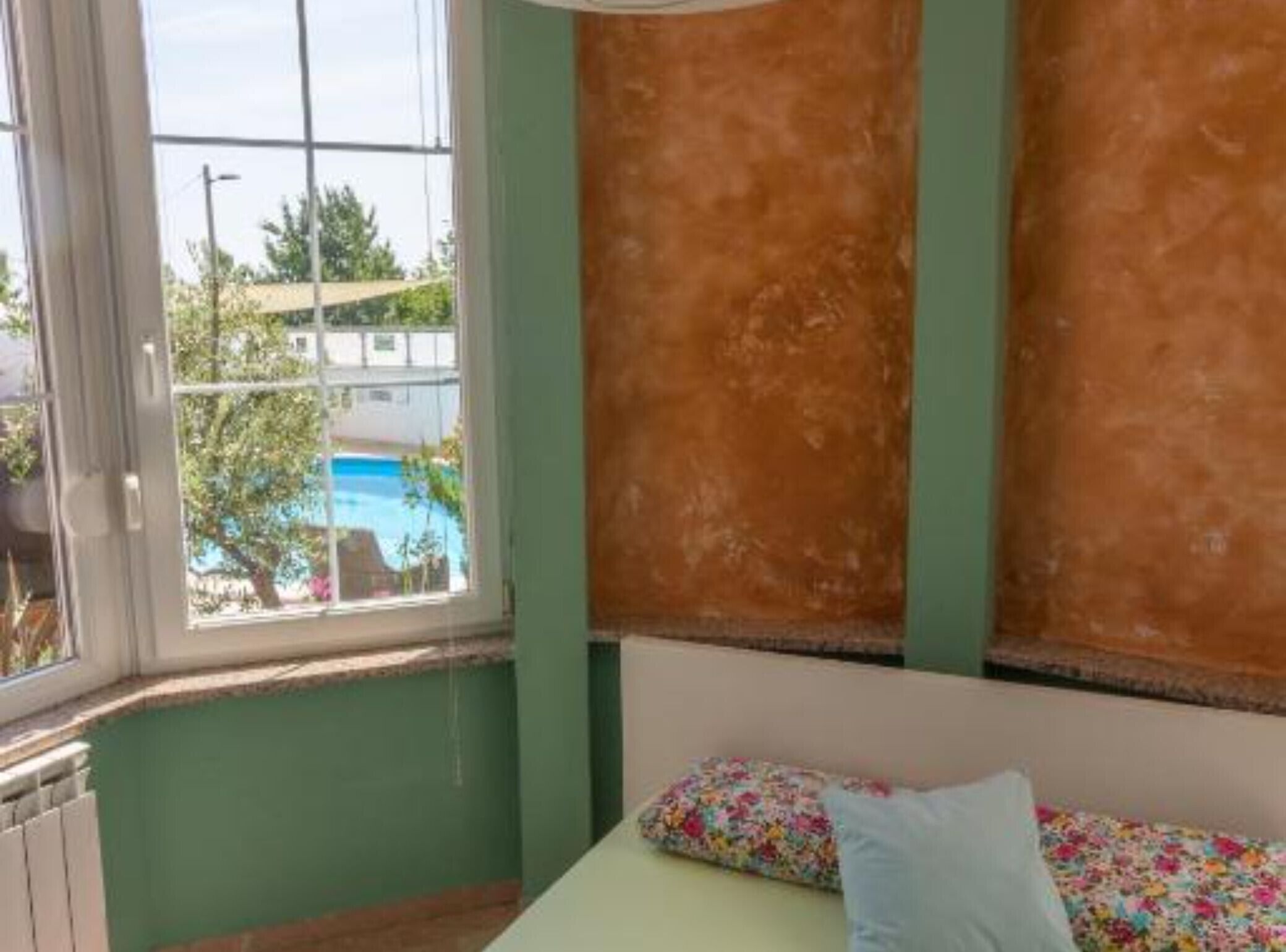 Un dormitorio con vistas a una piscina, una cama con ropa de cama floral y paredes verdes.