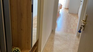 Un couloir avec une porte en bois, une plante en pot et un sol carrelé.