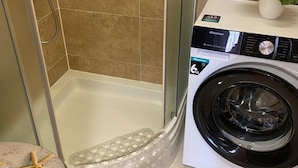Une petite salle de bain avec une douche en verre, un lave-linge et une petite plante en pot.