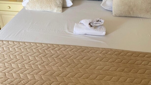 A bed with a textured headboard and a neatly made bed with two pillows and a folded towel.