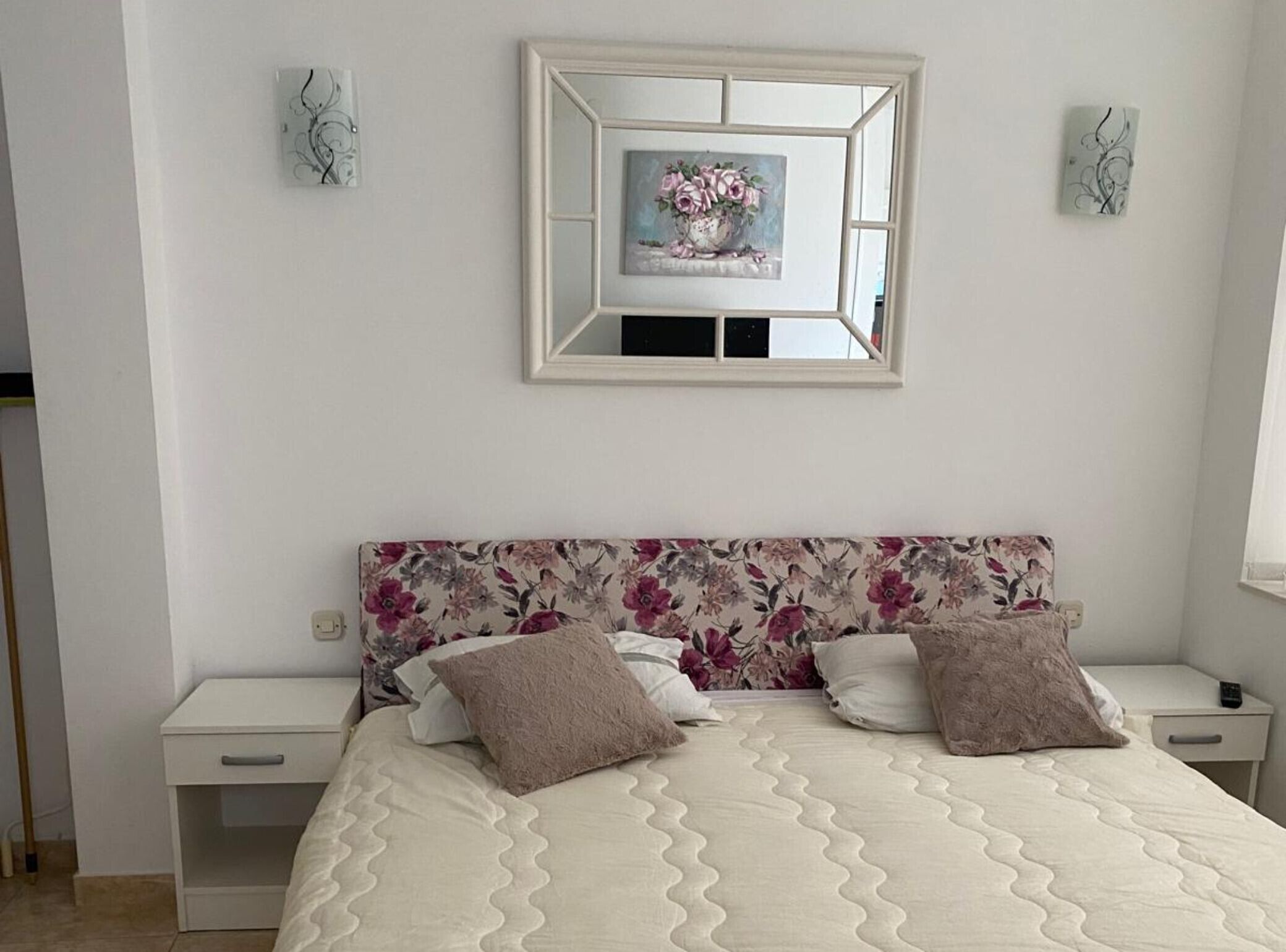 A bedroom with a bed, two nightstands, a mirror, and a floral headboard.