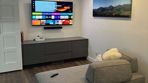 A modern living room with a flat-screen TV mounted on the wall, a grey sofa, and a painting of a mountain landscape. - Dog-Friendly Apt w/ EV Charger / Walk to Aspen (Aspen)