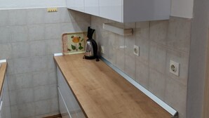 A kitchen with white cabinets, a wooden countertop, a kettle, and a decorative tile with a flower design. - Apartments Ivan Supetar - Two Bedroom Apartment with Terrace no.1 (Supetar)