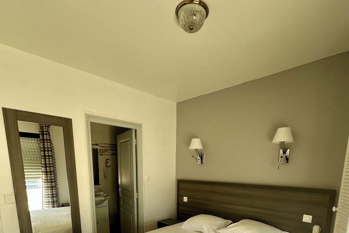 A bedroom with a large bed, a mirror, a bedside lamp, and a telephone.